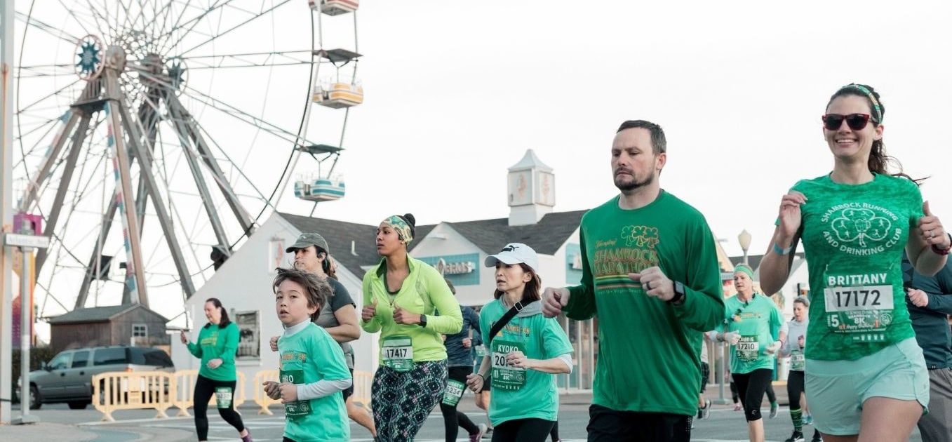 Participants running in green attire during the Shamrock Marathon, with a Ferris wheel in the background.