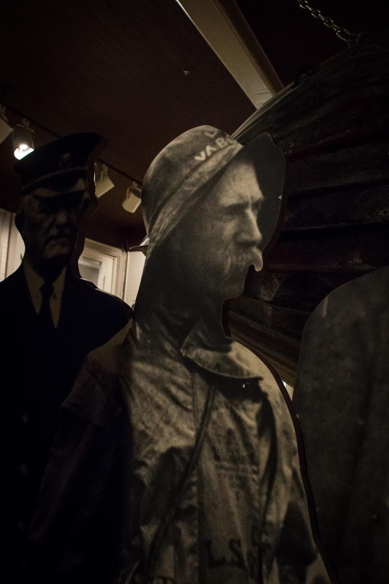 Cutout figures of people in maritime attire, including a sailor and fisherman, placed in a dimly lit exhibit space.