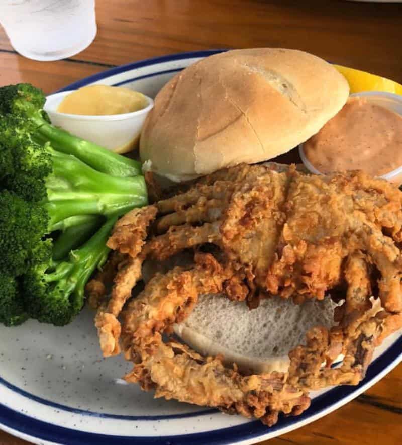 Plate with fried soft shell crab sandwich, broccoli, dipping sauce, and lemon wedge.