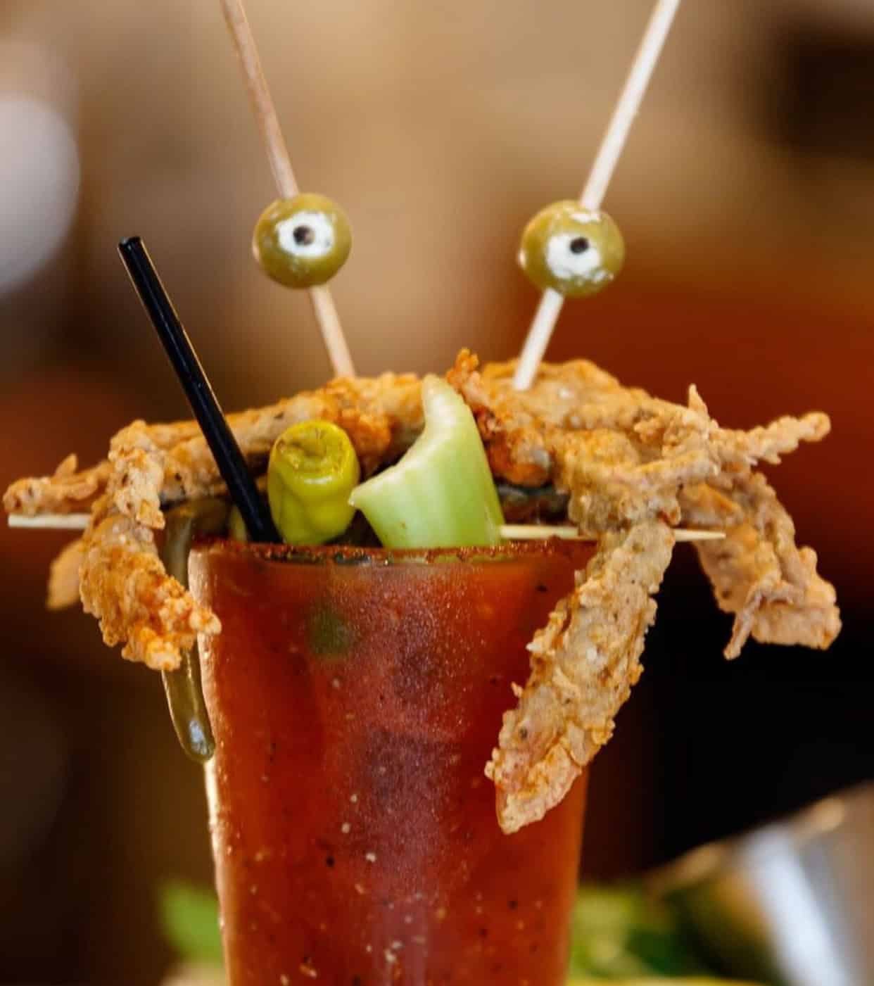 A Bloody Mary garnished with fried soft-shell crab, celery, olives, and peppers, with straws and skewers.