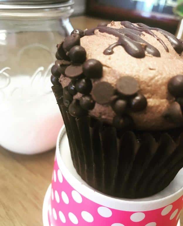 Chocolate cupcake with chocolate frosting and chips in a polka dot cup, next to a mason jar filled with sugar.