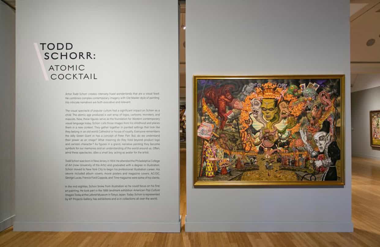 Museum display of Todd Schorr's "Atomic Cocktail" with explanatory text on the wall next to a colorful, detailed painting featuring various fantastical characters and elements.