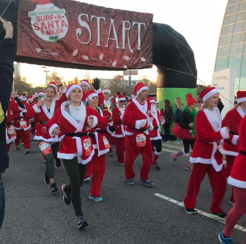 A group of people dressed in Santa costumes running at the start line of a race event.
