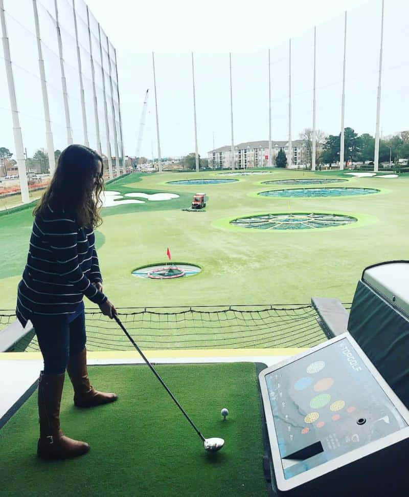 Person playing at an indoor driving range, preparing to hit a golf ball. Targets are visible on the field.