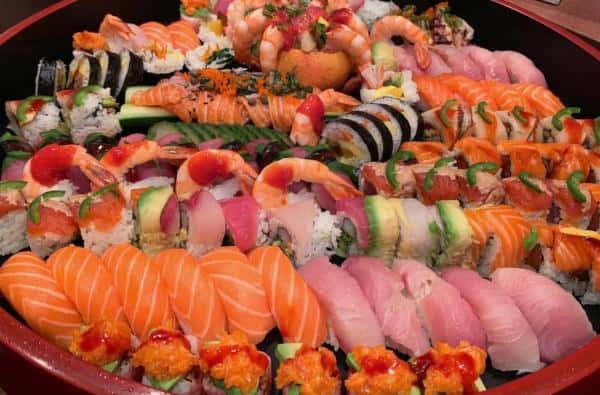 A platter filled with a variety of sushi rolls and nigiri, including salmon, tuna, shrimp, and avocado, garnished with sauces and herbs.