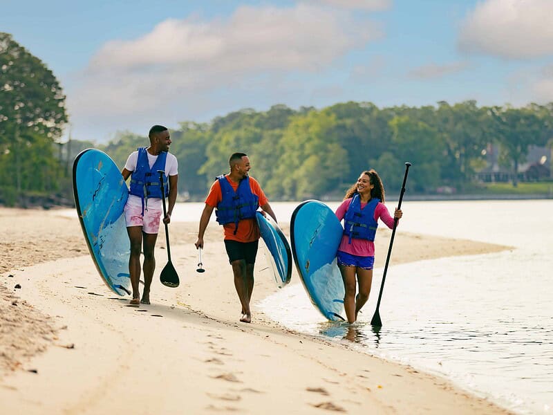 Three people at The Narrows carrying SUP boards on the beach.