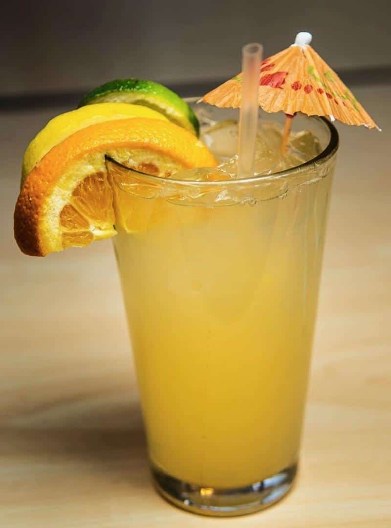 A tall glass of orange juice with ice, garnished with slices of orange, lemon, and lime, and a small paper umbrella.