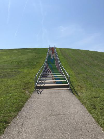 Staircase with colorful mural design leading up a grassy hill under a clear blue sky.
