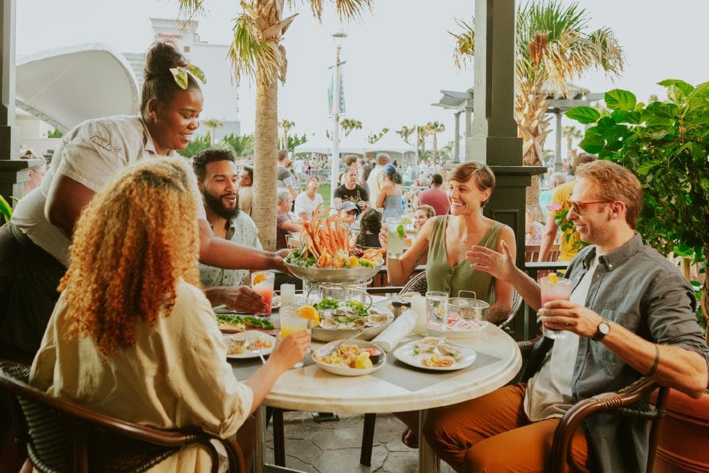 A diverse group enjoying a vibrant outdoor dining experience, with seafood dishes and cocktails at a restaurant.