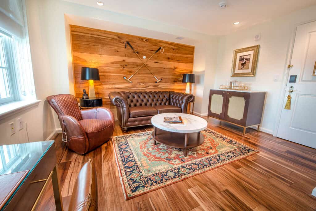 Elegant living room featuring a brown leather chesterfield sofa, vintage-style armchair, round marble coffee table, and wooden accents.