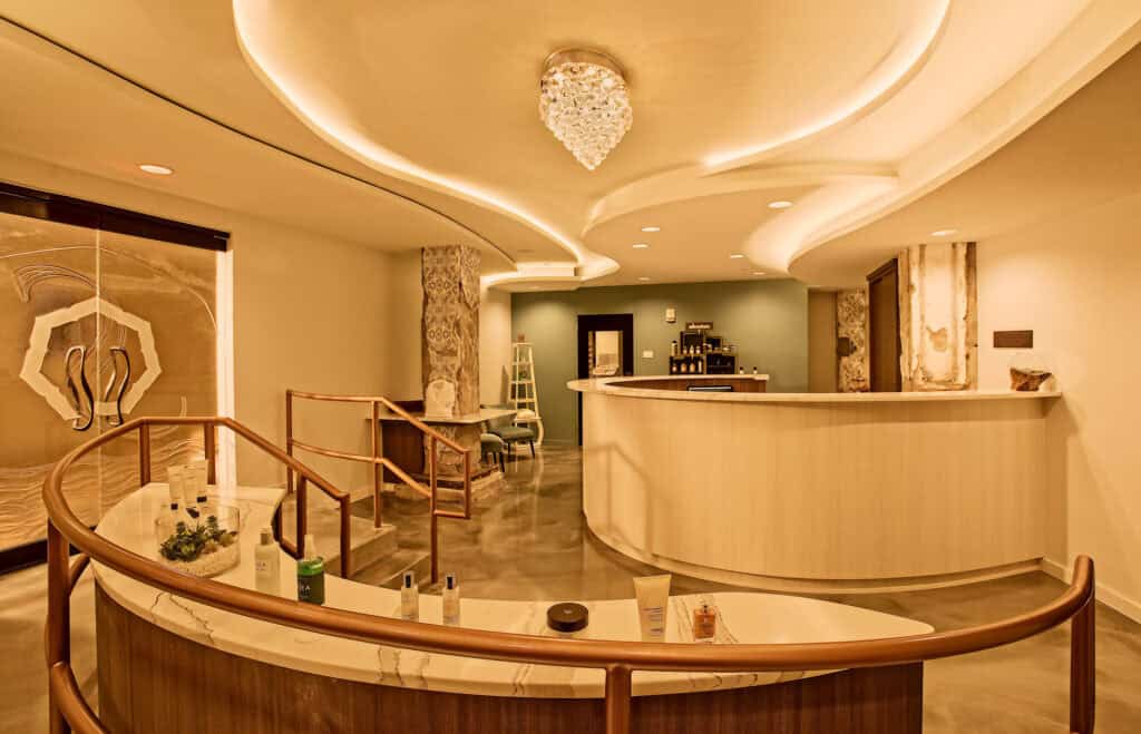 A stylish spa reception area featuring a curved front desk, decorative lighting, and skincare products displayed on a counter.