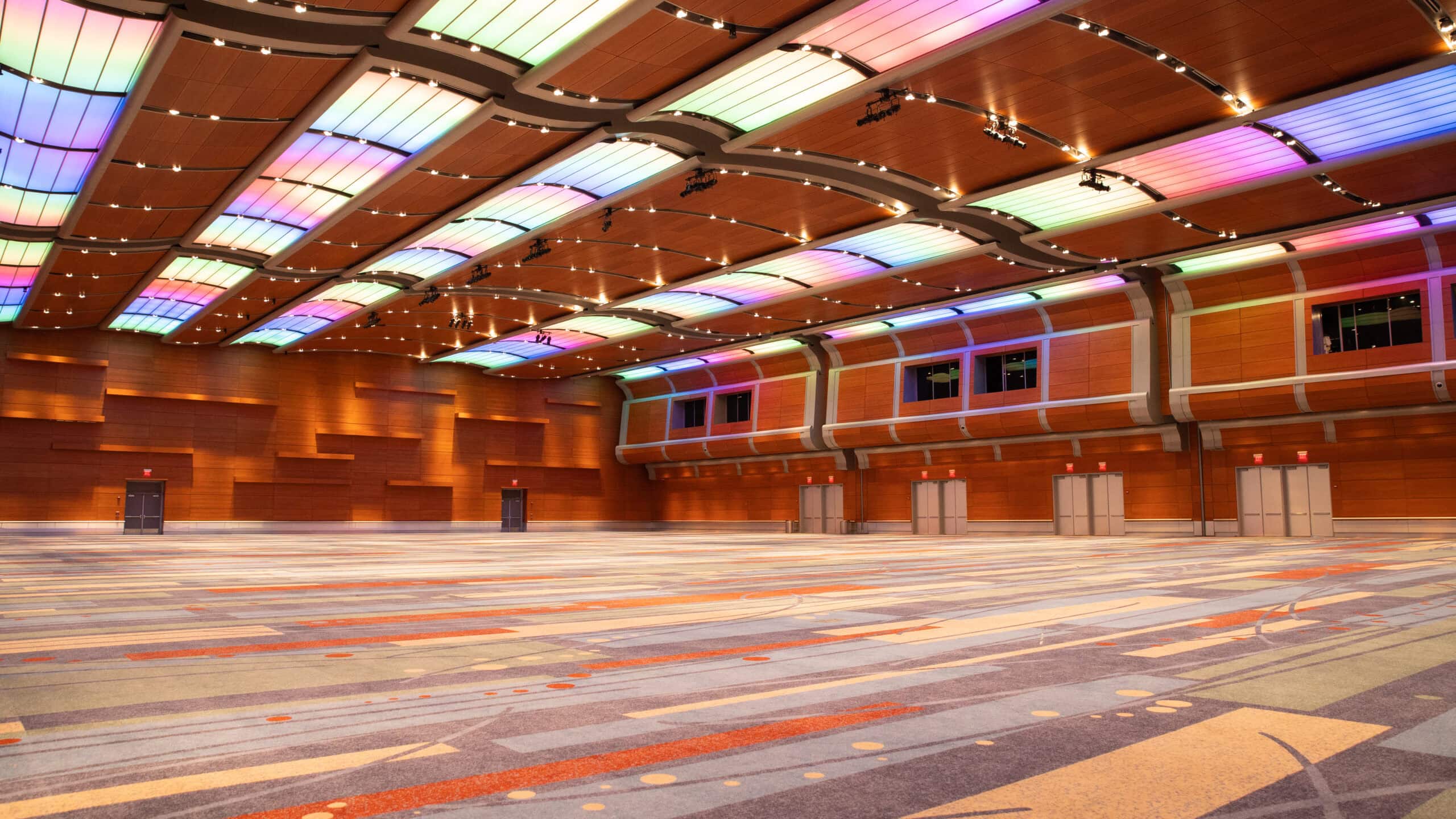 A spacious and modern event hall featuring colorful LED lighting, wooden walls, and patterned carpeting, ideal for gatherings.