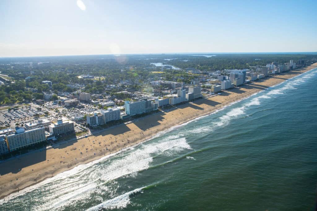 Aerial view of Virginia Beach with high-rise buildings along the shore, showcasing sandy beaches and ocean waves under a clear sky.