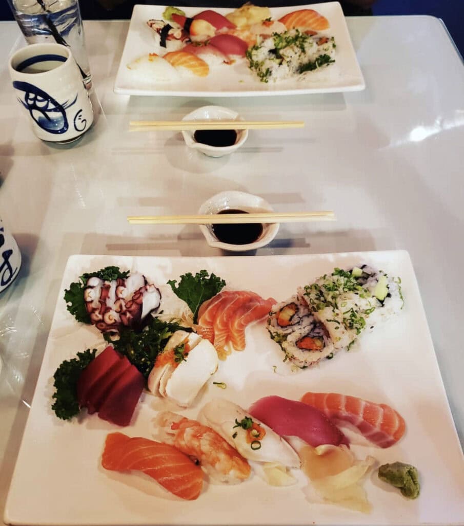 A beautifully arranged sushi platter featuring various types of sushi, sashimi, and soy sauce with chopsticks on a table.
