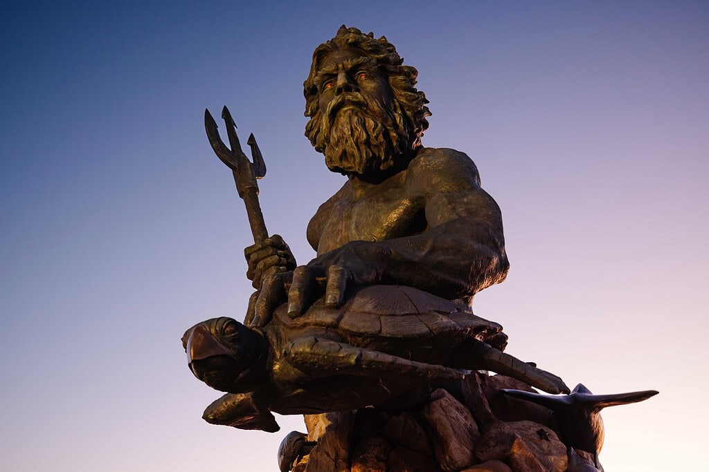 A close up view of the King Neptune Statue holding a trident and a turtle with a purple sunrise sky behind it in Virginia Beach.