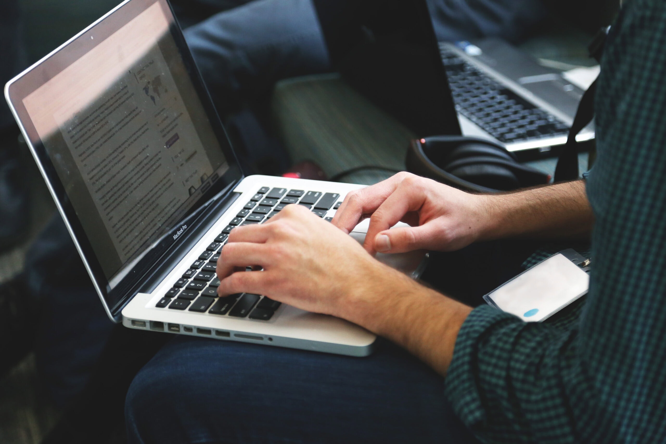 A person typing on a MacBook in a casual setting, with a focus on their hands and the laptop's screen.