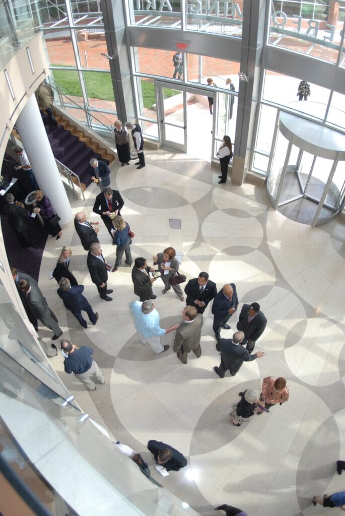 Aerial view of a bustling atrium with a group of people networking, dressed in business attire, on a patterned floor.