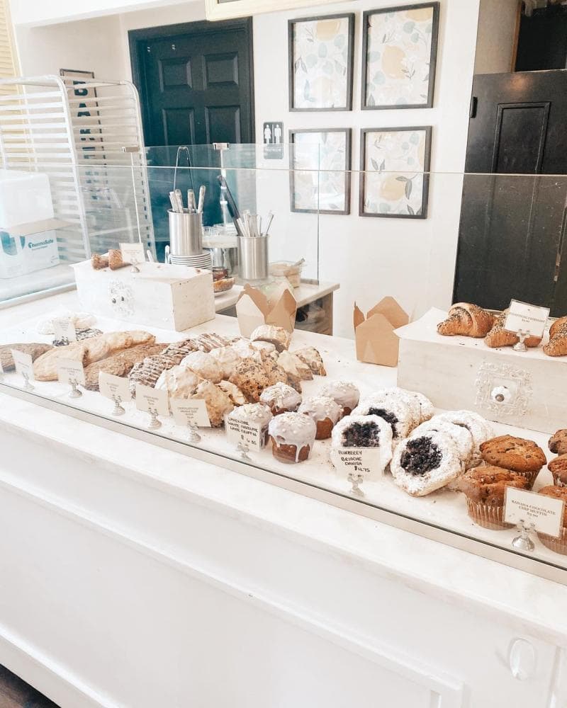 Bakery display with a variety of pastries and muffins behind a glass case. Labels are visible for each baked item.