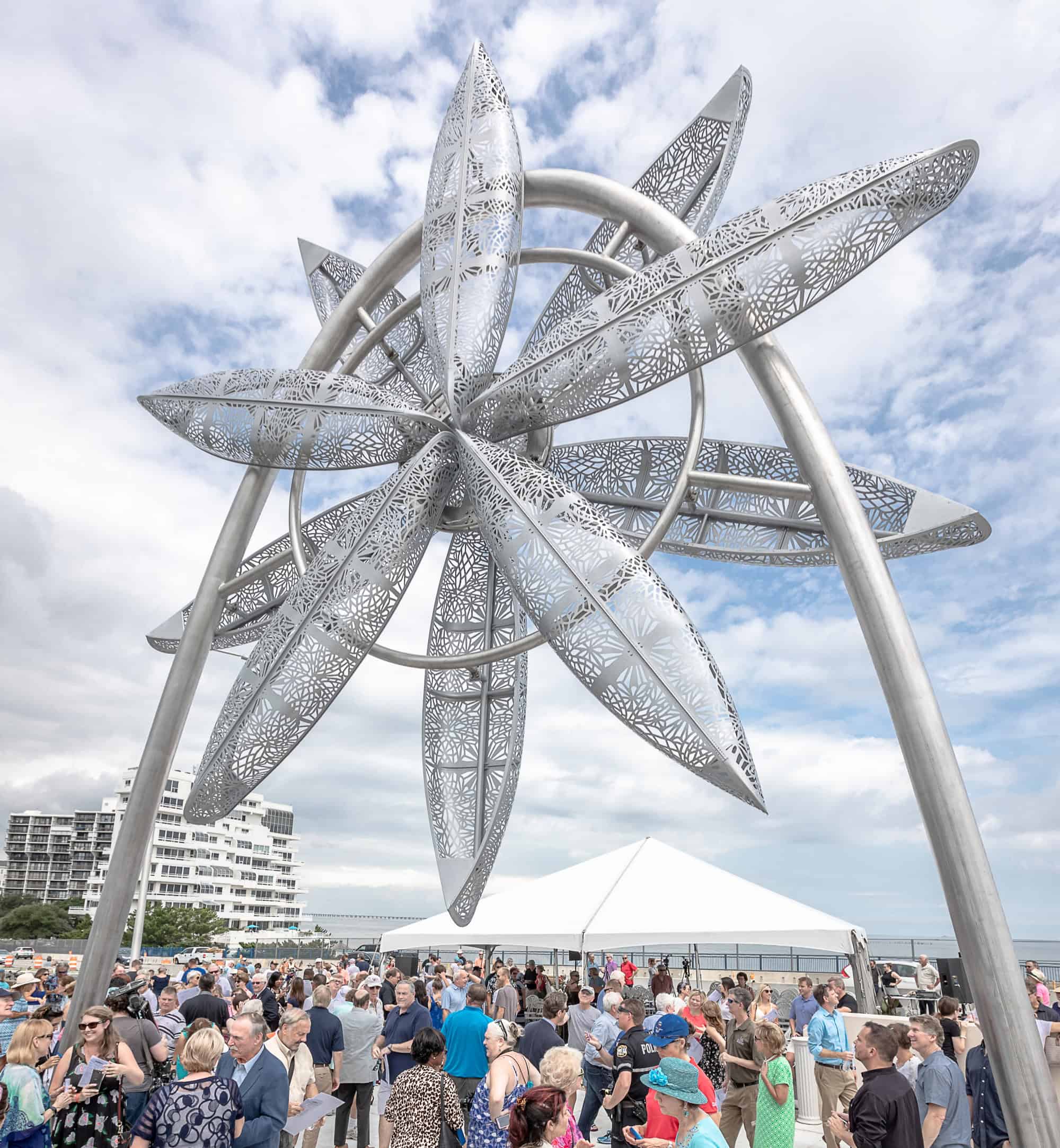 People gather around a large metal sculpture with interlocking elliptical shapes under a cloudy sky.
