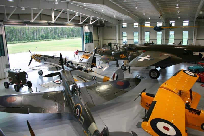 A collection of vintage military aircraft on display inside a large hangar, including various fighter planes and a bomber.
