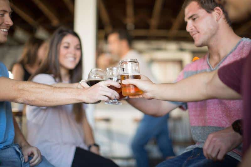 Four people clinking glasses filled with beer while smiling in a casual setting.