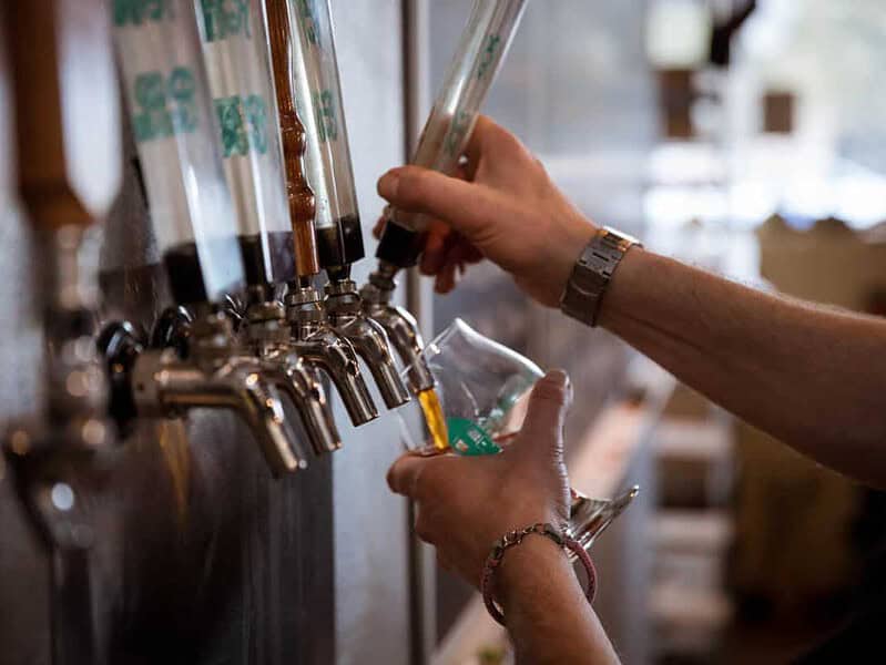 A person fills a glass with beer from a tap in a bar or brewery.
