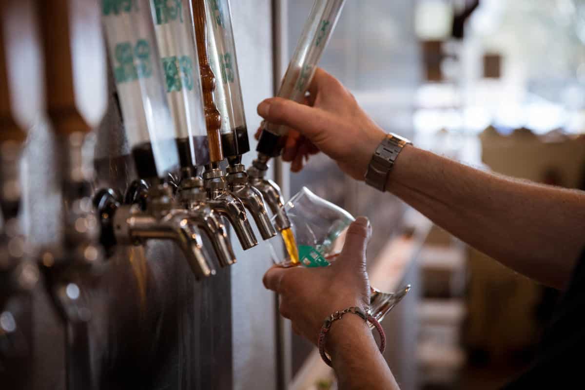 A person fills a glass with beer from a tap in a bar or brewery.