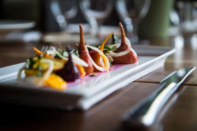 Gourmet dish with artfully arranged slices of vegetables, herbs, and sauce on a long white plate.