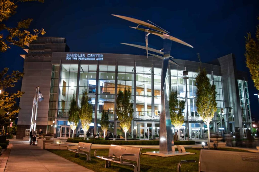 Night view of Sandler Center for the Performing Arts, featuring a modern glass facade and artistic sculpture in the foreground.