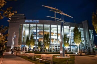 Exterior view of the Sandler Center for the Performing Arts at night, featuring modern architecture and a large metal sculpture in the foreground.