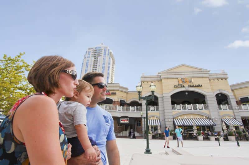 A family with a small child stands outside a large building labeled "Cucina Italiana" on a sunny day.