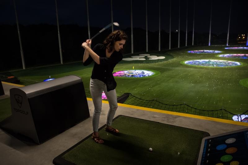 Person preparing to hit a golf ball at a driving range at night, with luminous targets in the distance.