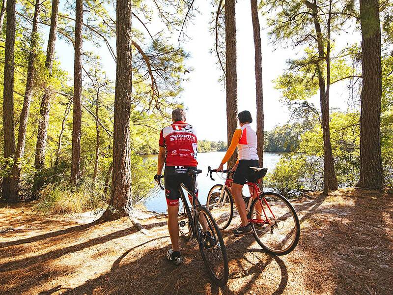 man and woman biking on a path in the woods overlooking freshwater