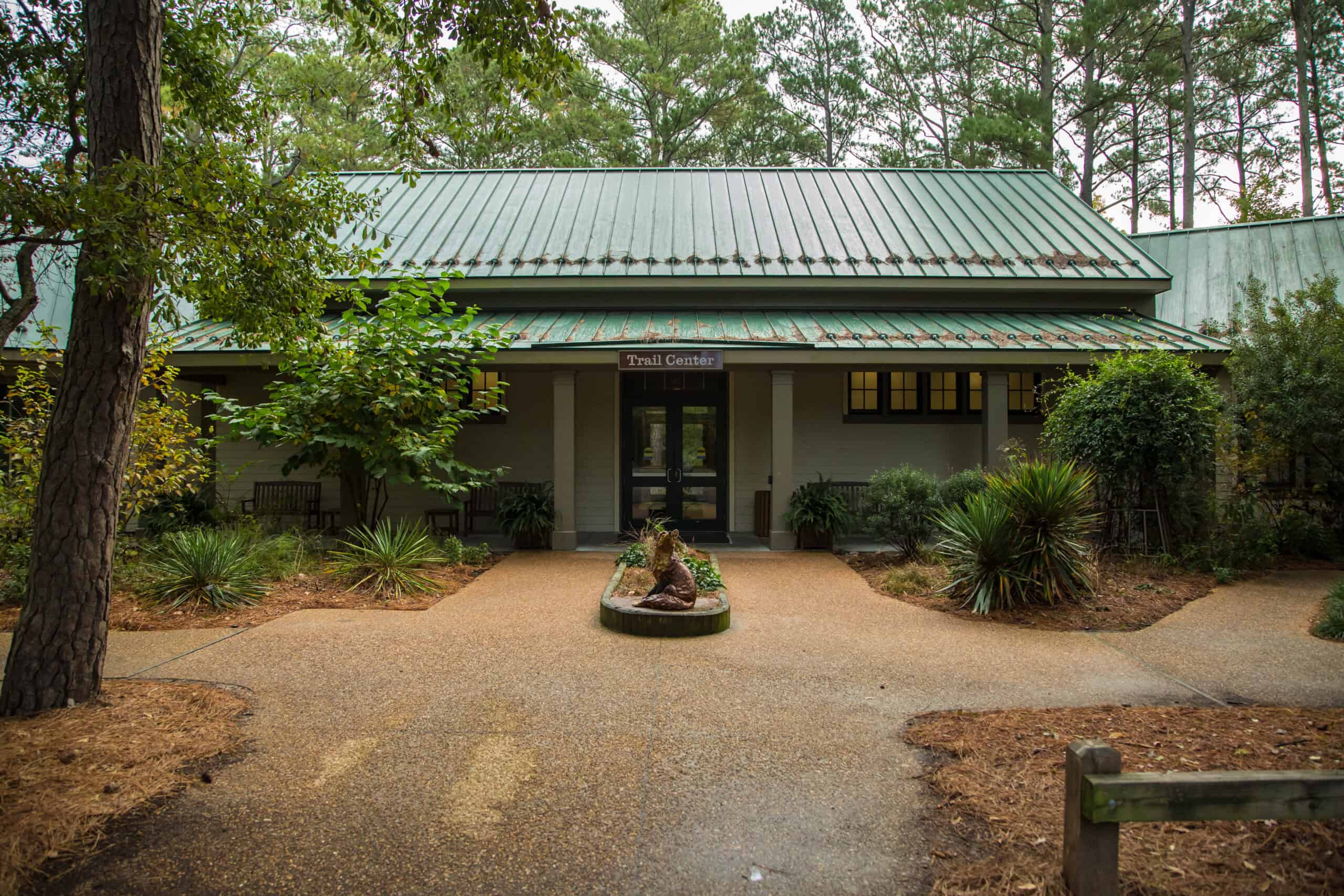 A green-roofed trail center surrounded by trees and shrubs on a cloudy day. Pathway leads to the entrance.