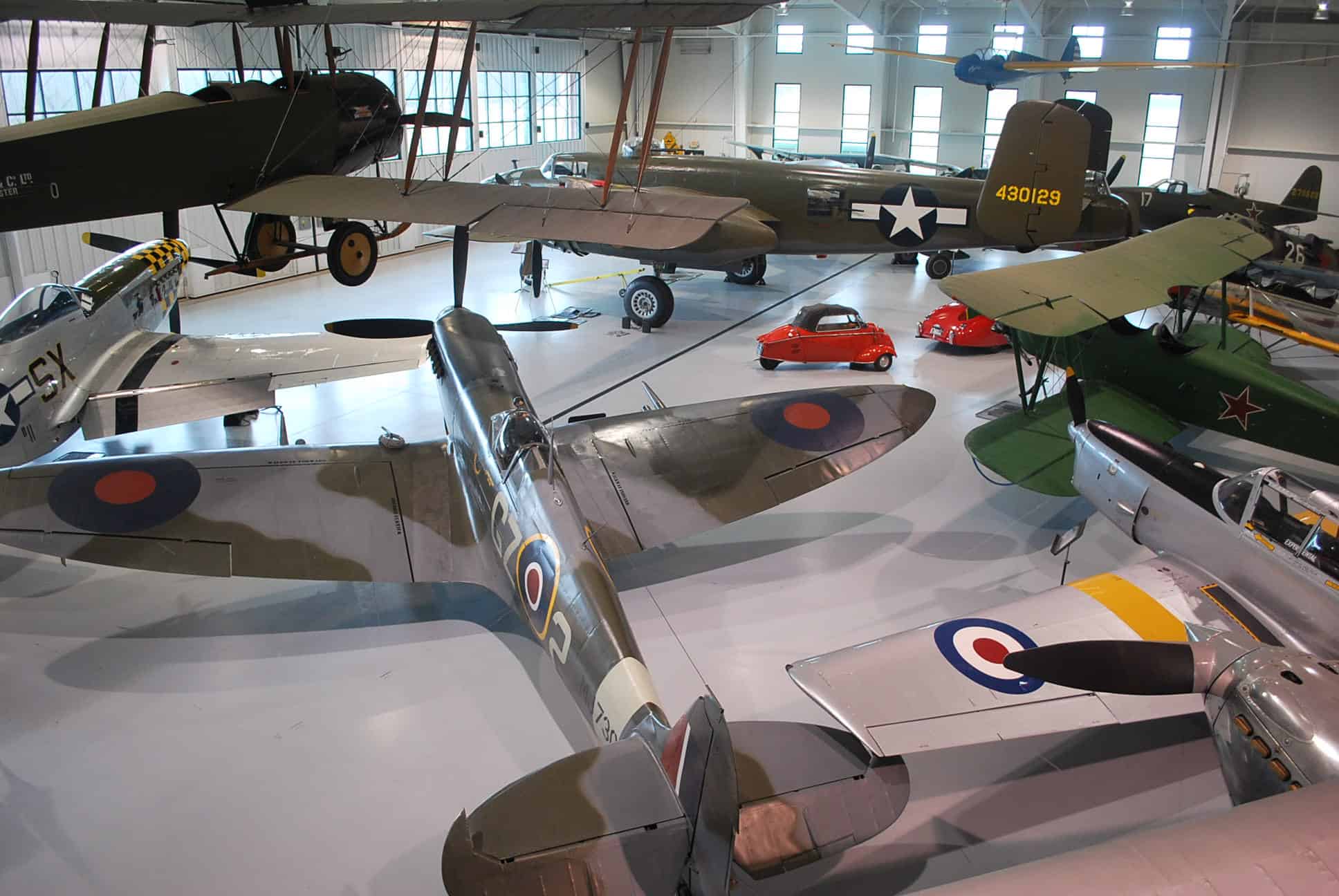 A collection of vintage military aircraft displayed in a museum hangar, including models with UK and US insignia.