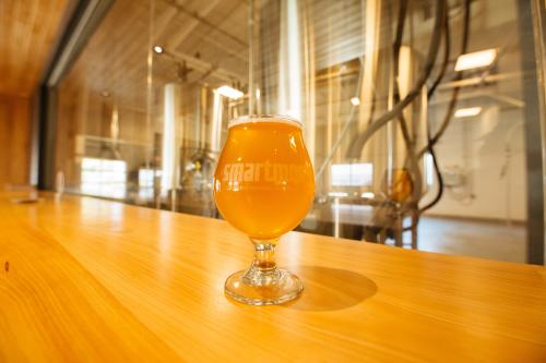 A glass of amber-colored beer on a wooden countertop in a brewery setting.