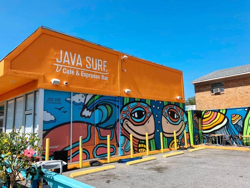 Bright orange cafe with vibrant mural art, labeled "Java Surf Café & Espresso Bar," in a sunny parking lot.