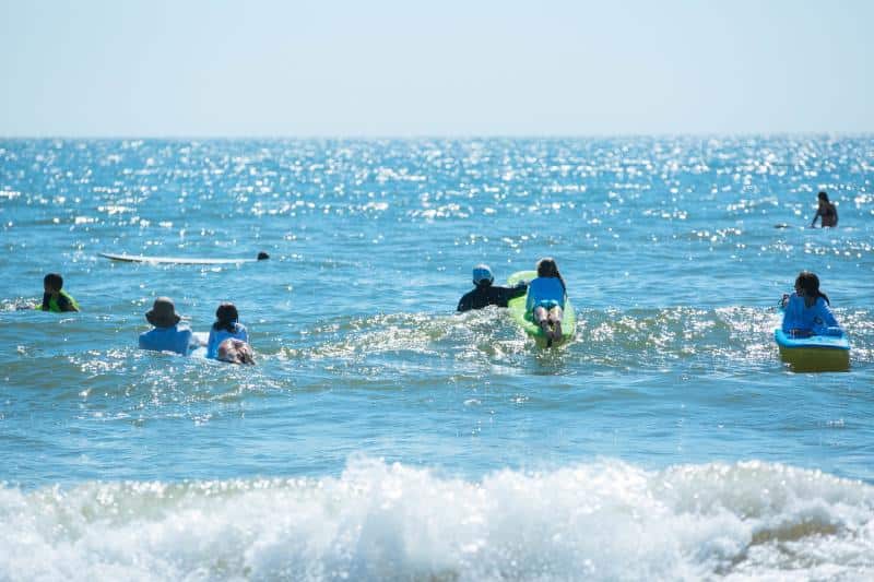 Several people are riding surfboards and bodyboards on the ocean waves on a sunny day.