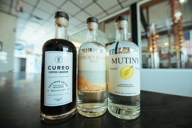 Three bottles are displayed on a counter: Cureo coffee liqueur, Chick's Beach rum, and Mutiny Island vodka, each with their respective labels visible.