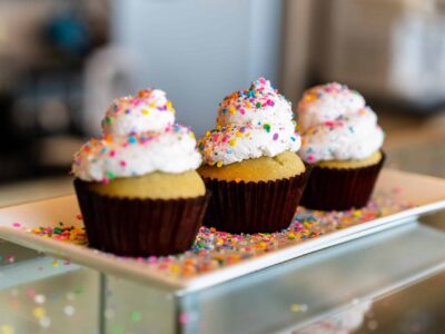 Three vanilla cupcakes with white frosting and colorful sprinkles on a rectangular white plate.