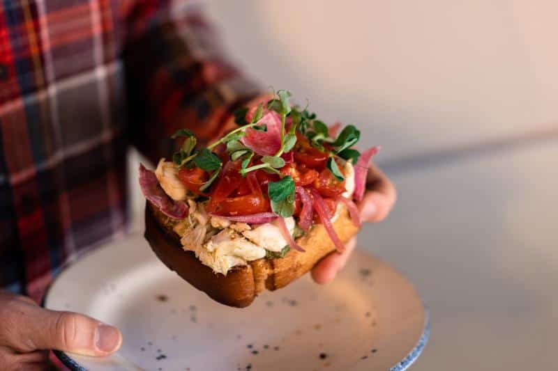 Person holding a plate with a toasted sandwich topped with greens, diced tomatoes, and red onions.