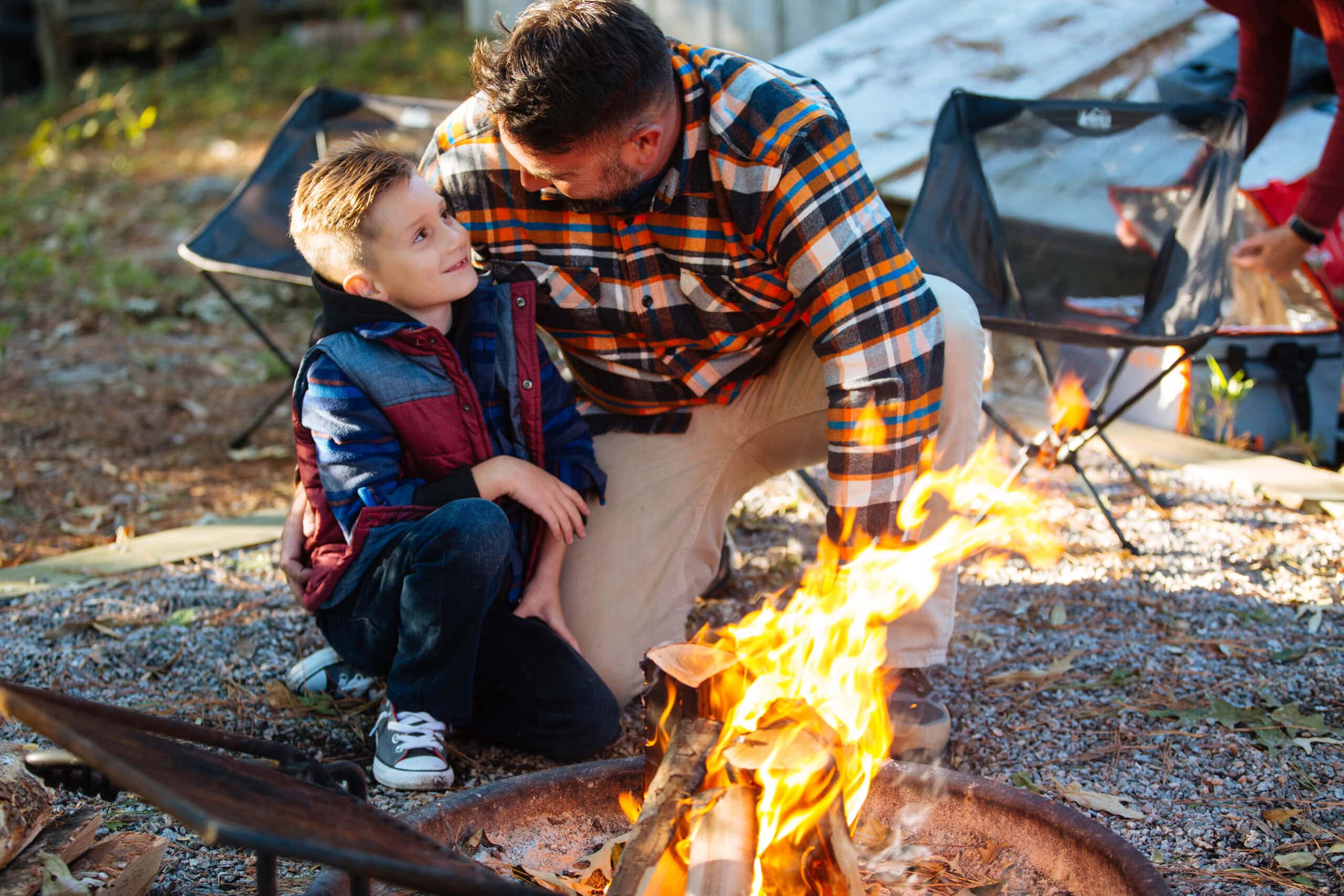 man and boy crouched over a firepit outside at a campground