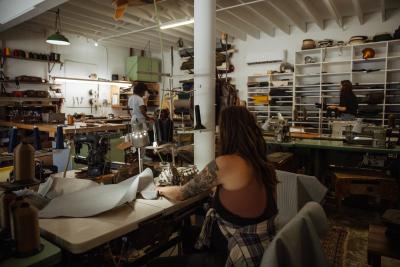 People working in a cluttered workshop with sewing machines, fabrics, and shelves filled with materials.
