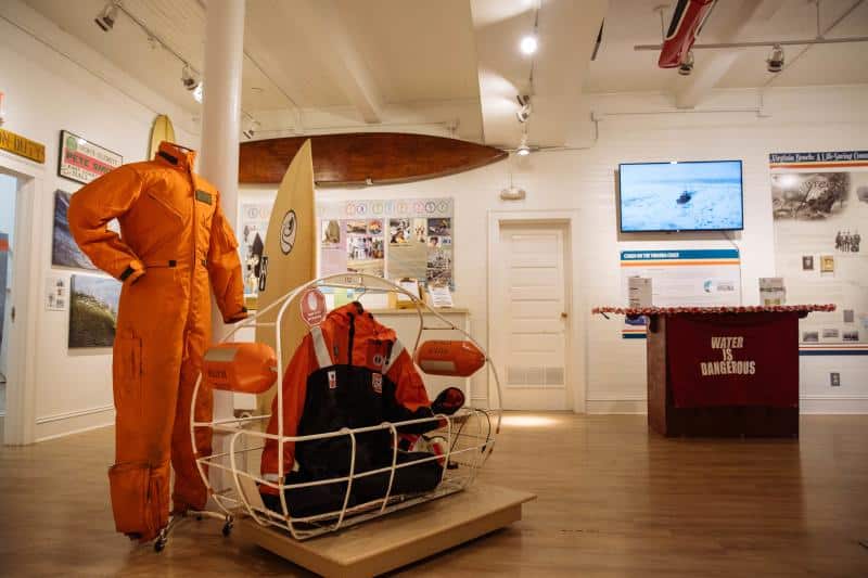 The Virginia Beach Surf and Rescue Museum exhibit featuring an orange survival suit, rescue equipment, and informational displays on walls about water safety and history.