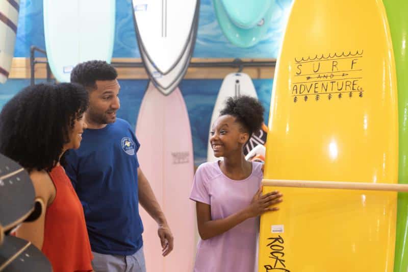 Family looking at a bright yellow surfboard in a store, with other surfboards displayed in the background.