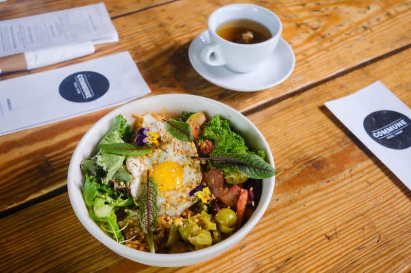 A bowl of salad with a fried egg on top, accompanied by a cup of tea on a wooden table.