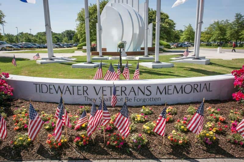 Tidewater Veterans Memorial with American flags and flowers in front, commemorating veterans with the inscription "They Shall Not Be Forgotten.