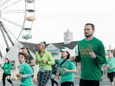 Participants running in green attire during the Shamrock Marathon, with a Ferris wheel in the background.