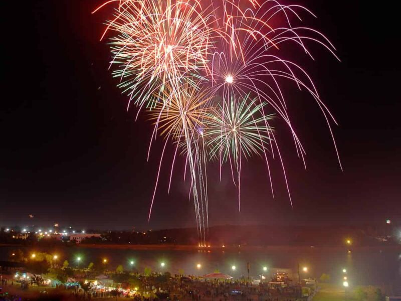 Fireworks light up the night sky over Virginia Beach, with a crowd gathered below.