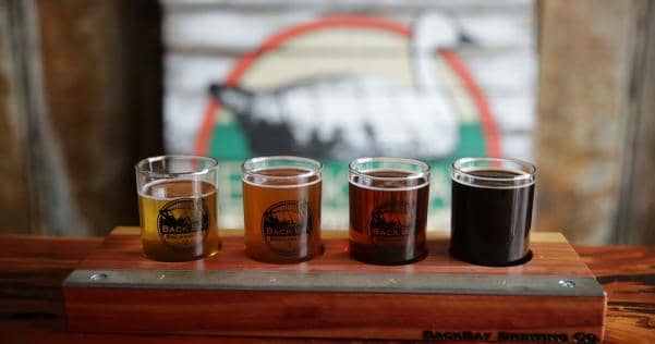 Four glasses of beer in a wooden flight holder on a table.